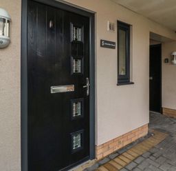 A black front door with small windows and mail slot on a beige wall with a light fixture and a window at Greenlee House in Seahouses