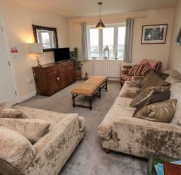 A living room with two sofas a striped armchair a long upholstered bench a wooden cabinet with a TV a window with curtains and a framed picture on the wall at Greenlee House in Seahouses