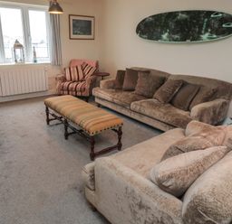 A living room with two sofas a striped armchair a long bench a surfboard mounted on the wall and a window with curtains at Greenlee House in Seahouses