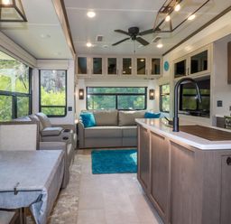 An interior space with a kitchen island a sofa with blue pillows large windows and a dining table at Tickeydoo Tor Down Quarry in St Breward