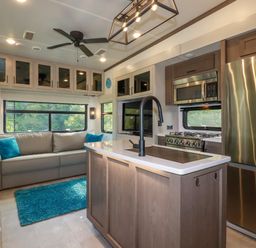 A kitchen and living area with a gray sofa, blue rug, kitchen island with black faucet, stainless steel refrigerator and stove at Tickeydoo, Tor Down Quarry in St Breward
