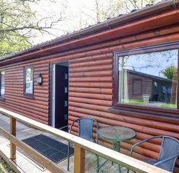 A wooden cabin exterior with windows a door and outdoor table with chairs at The Blacktail in Llanerch Park near St Asaph