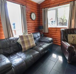 A room with leather sofa and armchair with pillows wooden walls and tiled floor at The Blacktail in Llanerch Park near St Asaph