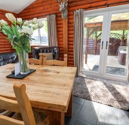 A dining area with a wooden table and chairs a vase of flowers a leather armchair curtains and glass doors at The Blacktail in Llanerch Park near St Asaph