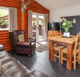 A living area with a leather armchair a wooden dining table with chairs a television and sliding glass doors at The Blacktail Llanerch Park near St Asaph