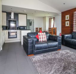 A living room with two black leather sofas a gray rug and an open kitchen area at The Buck in Llanerch Park near St Asaph