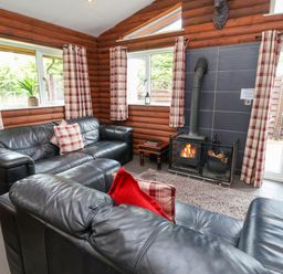 A living room with black leather sofas a fireplace and plaid curtains at The Buck in Llanerch Park near St Asaph