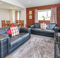 A living room with two black leather sofas and a dining table with wooden chairs at The Buck in Llanerch Park near St Asaph