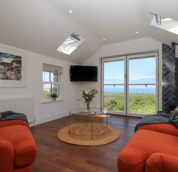 A living room with two orange sofas a glass coffee table and a wood burning stove at Victory View in Pendeen
