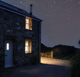 A stone house with lit windows under a starry sky at Victory View in Pendeen