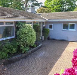 An outdoor paved driveway area with shrubs and a building with windows and a tiled roof at Sweden Bridge Cottage in Ambleside