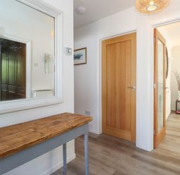 A hallway with a wooden table and a large wall mirror next to a closed wooden door and an open door leading to a living room at Sweden Bridge Cottage in Ambleside
