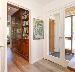 A hallway with wooden floor a glass door a wooden cabinet with books and a map on the wall at Sweden Bridge Cottage in Ambleside