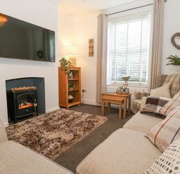A living room with a sofa an armchair a television mounted on the wall and a small fireplace at Garibaldi Cottage in Weymouth