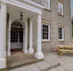 The entrance of a stone building with white columns and a wooden picnic table on the patio at Llwynderw Hall in Abergwesyn near Llanwrtyd Wells