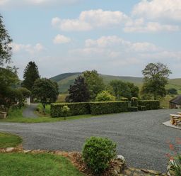 A gravel driveway leading to a garden area with trimmed hedges trees hills in the background at Llwynderw Hall in Abergwesyn near Llanwrtyd Wells