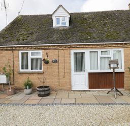 The exterior front view of a brick house with a mossy roof several potted plants a birdhouse white doors and windows at Ground Floor Annex in Milton-Under-Wychwood