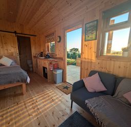 A wooden interior room with a bed sofa kitchen area and a door leading outside at Hafan Gelli Sheperds Hut - Tudwal in Pwllheli