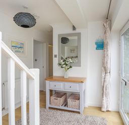 An entryway with a wooden table with drawers and baskets below a mirror a hanging light and a window with curtains at Mor Glas in Abersoch