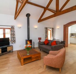 A living room with a wood burning stove and wooden beams at Woodland Roost in Parkham near Bideford