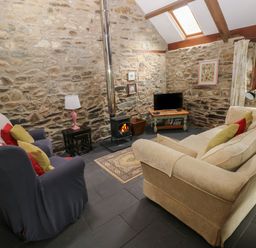 A living room with stone walls a wood stove a TV two couches and a window at The Old Stable in Pontfaen near Fishguard