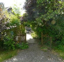A garden path with a wooden gate and chairs visible through foliage at The Old Stable in Pontfaen near Fishguard