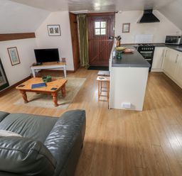 A living room with a wooden coffee table a TV a stove and a kitchen area at The Loft in Pontfaen near Fishguard