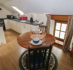 A kitchen with a round wooden dining table set for two beside a window with floral curtains at The Loft in Pontfaen near Fishguard