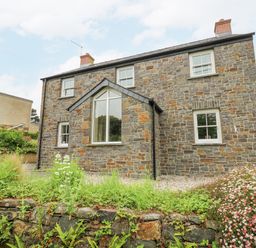A stone house with white framed windows and a garden with flowers at Beachway in Brynhenllan near Dinas Cross
