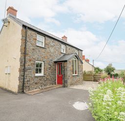 Stone house with red door driveway and flowering plants at Beachway Brynhenllan near Dinas Cross