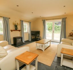 A living room with two cream sofas wooden coffee and side tables a television and blue curtains at Beachway Brynhenllan near Dinas Cross