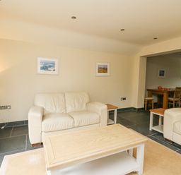 A living room with beige sofas wooden coffee table side tables lamp and wall pictures at Beachway in Brynhenllan near Dinas Cross