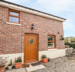 The front entrance of a brick house with a wooden door and three windows with flower pots outside at Field View in Llanybydder