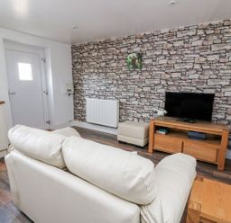 A living room with a white sofa a wooden TV stand with a television a small ottoman and a stone effect feature wall at Field View in Llanybydder