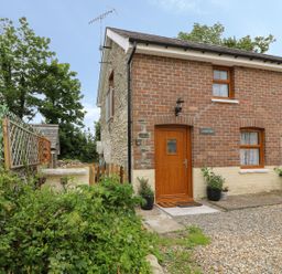 A brick and stone house with wooden door and windows surrounded by plants and gravel at Garden View in Llanybydder