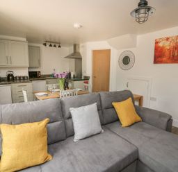 A living room with a gray sofa and yellow pillows next to an open kitchen and dining table with flowers at Garden View in Llanybydder