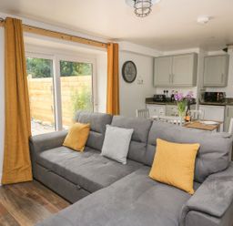 A living room with gray sofa and yellow pillows next to a dining table and kitchen at Garden View in Llanybydder