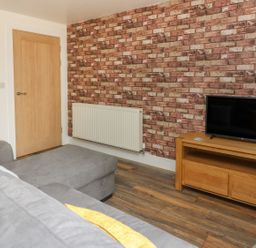 A room with a gray sofa a wooden door a radiator and a TV on a wooden stand at Garden View in Llanybydder
