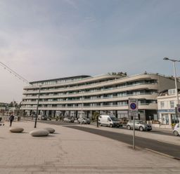 A modern apartment building with balconies along a street with parked cars and a tiled walkway with round stone benches at Apartment 17 Abbey Sands in Torquay