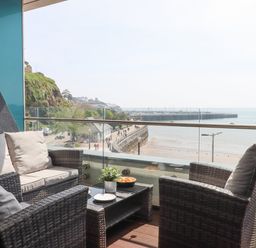 A balcony with wicker chairs and a table overlooking a beach and a pier at Apartment 17 Abbey Sands in Torquay