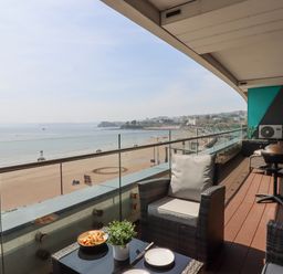 A balcony with chairs a table a small plant and food overlooking the beach and sea at Apartment 17 Abbey Sands in Torquay