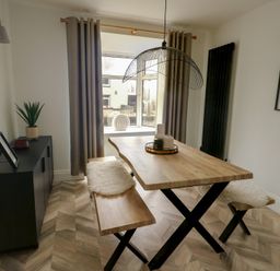 A dining room with wooden table and benches near a window with curtains at 1 Mona Terrace in Llanfachraeth