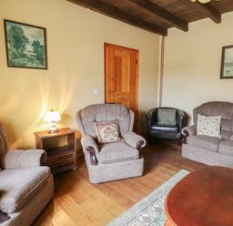 A living room with armchairs a sofa a wooden coffee table a side table with lamp and paintings on walls at Castell Y Garn near Newport Beach Pembrokeshire