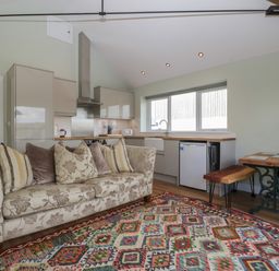 A living room with a patterned sofa and colorful rug next to a kitchen with cabinets and a dining table at Doubletree Cottage in Swainsford near Mere