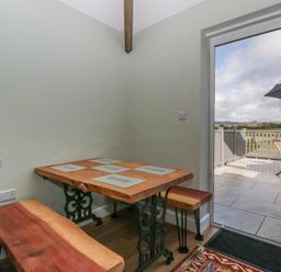 A corner dining area with a wooden table and benches next to a glass door leading to a patio with outdoor furniture at Doubletree Cottage in Swainsford near Mere