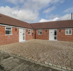 A courtyard with gravel and two brick buildings with tiled roofs and white doors at Singletree Cottage in Swainsford near Mere