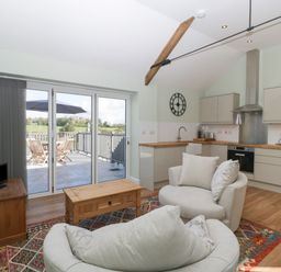 A kitchen and living area with armchairs a wooden coffee table a television and glass doors leading to an outdoor patio at Singletree Cottage in Swainsford near Mere