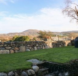 A garden with a stone wall and shed at Yr Hen Felin in Dyffryn Ardudwy