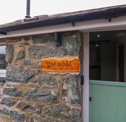 A stone wall with a wooden sign reading Y Stabl and a partially open green door at Y Stabl in Dyffryn Ardudwy