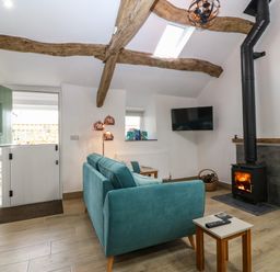 A living room with a teal sofa a wood burning stove a wall mounted television and a half door at Y Stabl in Dyffryn Ardudwy